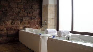 Un baño con dos bañeras, una pared de piedra y un ventanal grande.