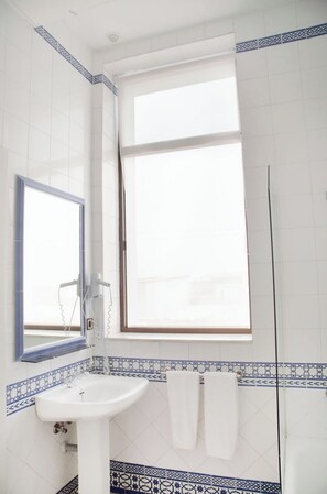 Un baño con lavamanos blanco, espejo y ventana con marco azul.