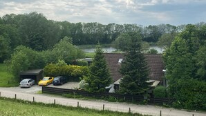 Un quartiere residenziale con una casa, auto parcheggiate e un fiume sullo sfondo.