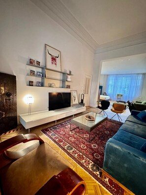 A modern living room with a flat-screen TV, a coffee table, and a blue sofa. - La Pièce appartement (Brussels)