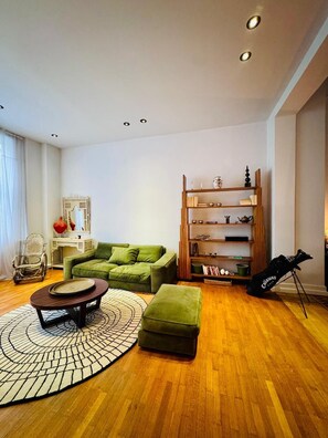 A modern living room with a green sofa, a wooden bookshelf, and a golf bag. - La Pièce appartement (Brussels)