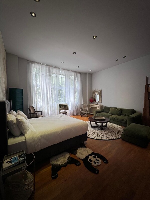 A modern bedroom with a large bed, a green sofa, a round coffee table, and a desk. - La Pièce appartement (Brussels)
