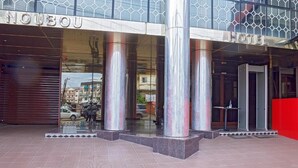 Das äußere Erscheinungsbild des NouBou Hotels mit großen, metallischen Säulen, einem Glastürbereich und einer roten Wand auf der rechten Seite.