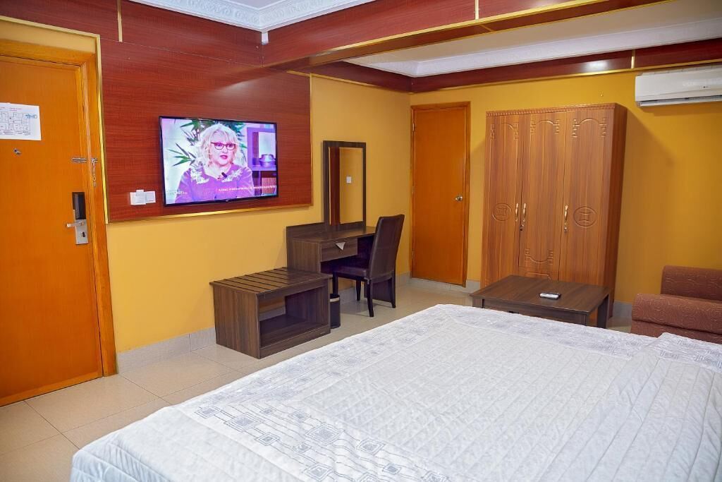 Een hotelkamer met een bed, een bureau met stoel, een kledingkast en een aan de muur bevestigde televisie.