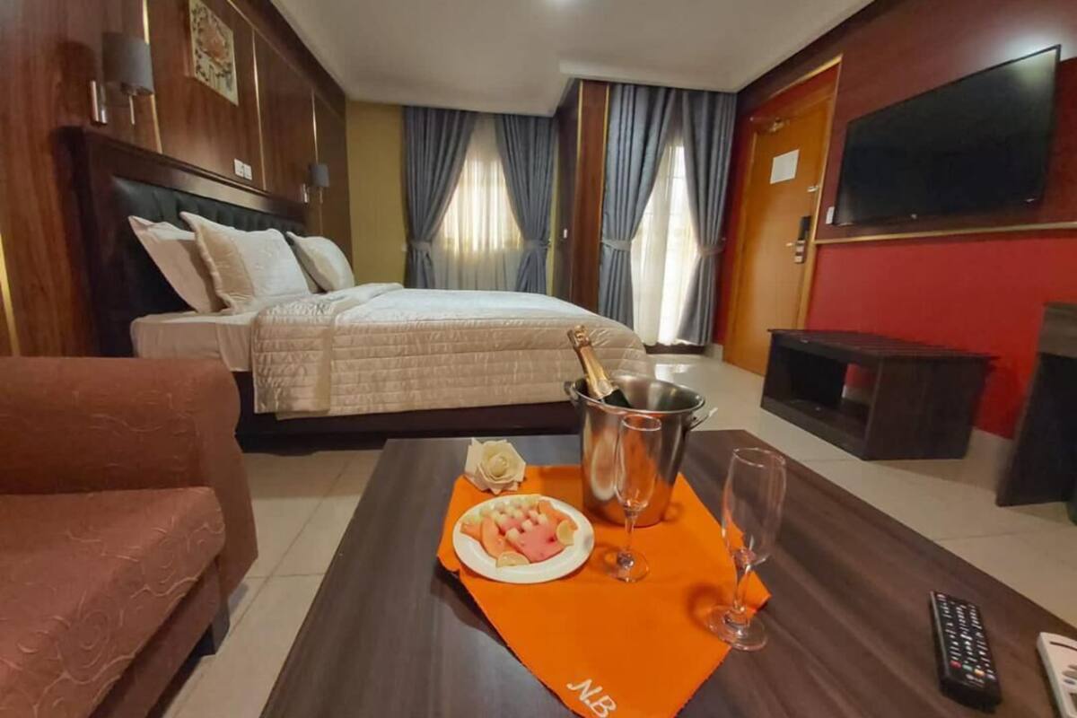 Une chambre d’hôtel avec un lit, une télévision, un meuble pour la télévision, une table basse avec une assiette de nourriture, une bouteille de champagne et une télécommande.