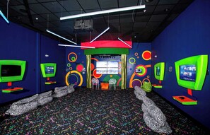 Una habitación con varias estaciones de videojuegos, un diseño de pared colorido y una alfombra estampada.