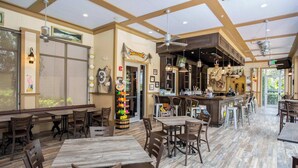 A spacious restaurant with wooden tables and chairs, a bar area, and a large window offering a view of the outdoors.