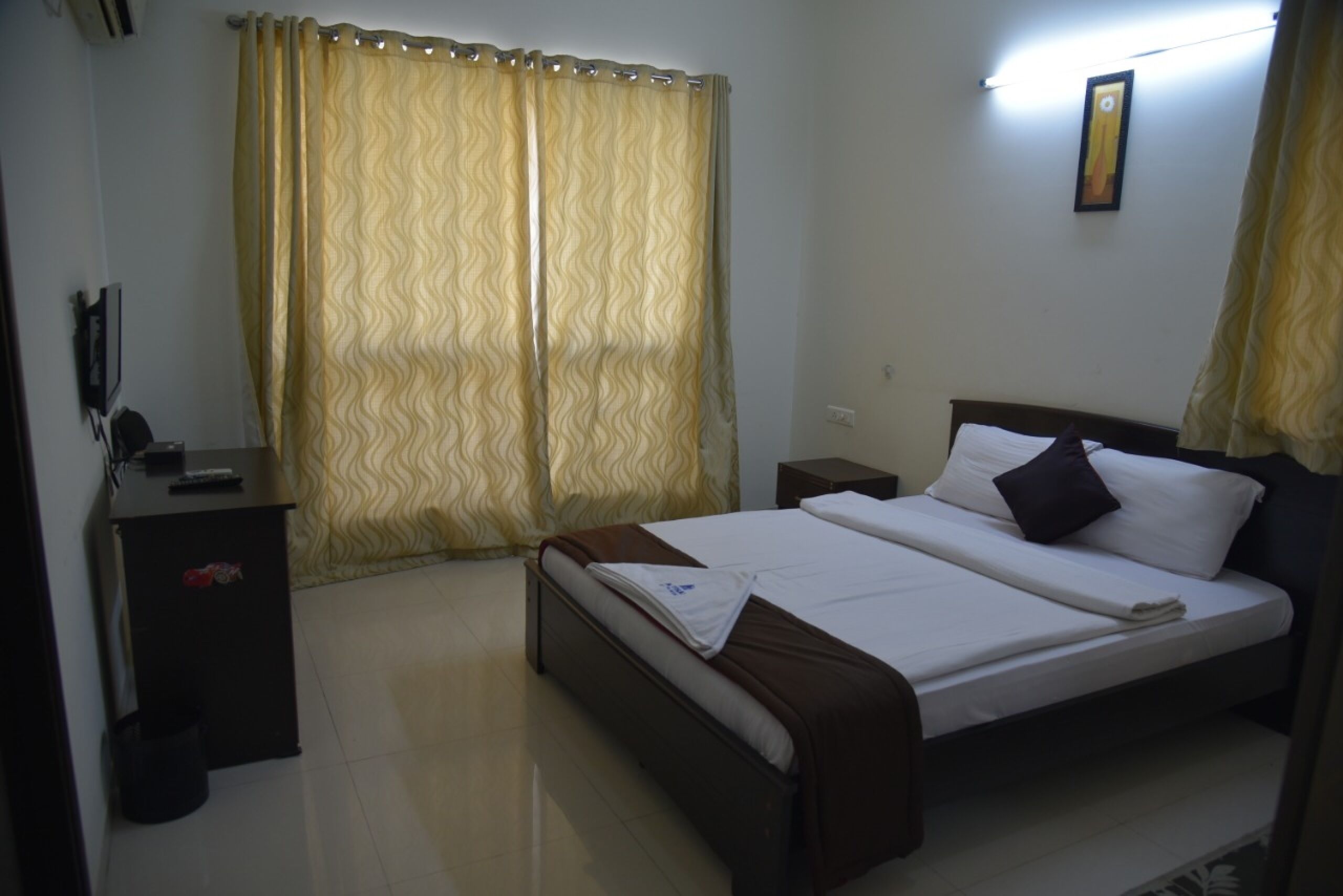 A neatly arranged hotel room with a bed, bedside table, and a small desk with a chair.
