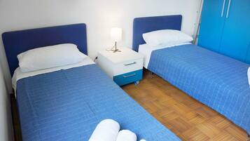 Une chambre avec deux lits, chacun doté d’une tête de lit bleue et d’une parure de lit assortie, également bleue. Une table de chevet blanche avec une lampe se trouve entre les deux lits.