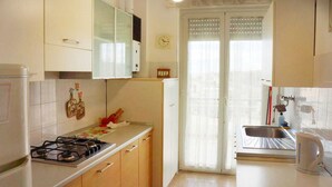 A kitchen with a gas stove, a sink, and a window with curtains. - Cleo Girasole (Porto Recanati)