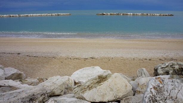 A beach with white rocks in the foreground and calm blue waters in the background. - Cleo Girasole (Porto Recanati)