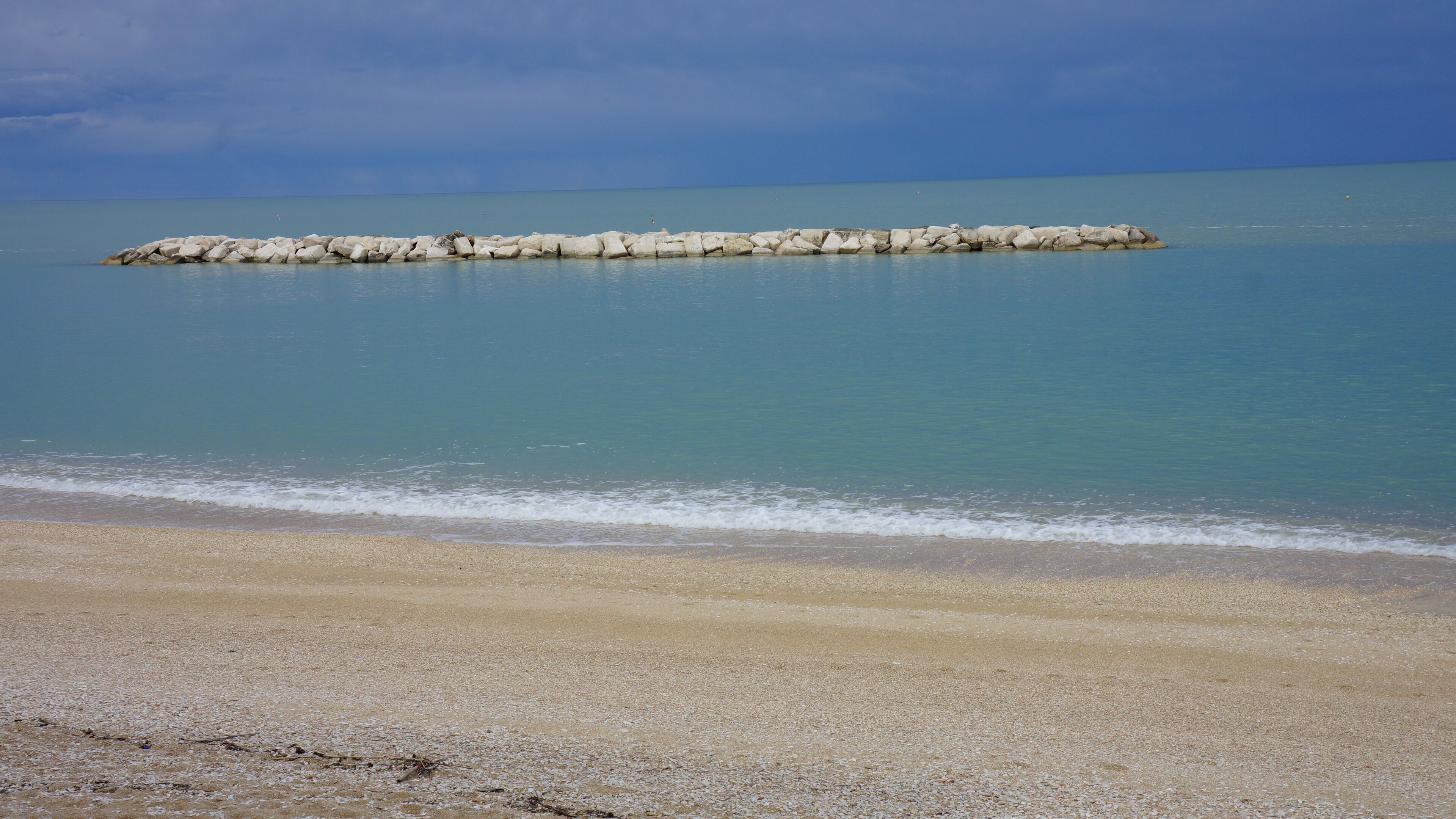 Een strand met een rotsachtige zeewering die zich uitstrekt over kalm, blauw water.