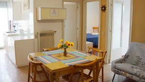 A dining area with a table set for four, a vase with sunflowers, and a view into a bedroom with a bed and a window. - Cleo Girasole (Porto Recanati)