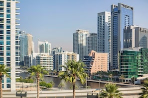 A cityscape with modern high-rise buildings, palm trees, and a river. - Famous Address Beach Resort JBR 1BR (Dubai)