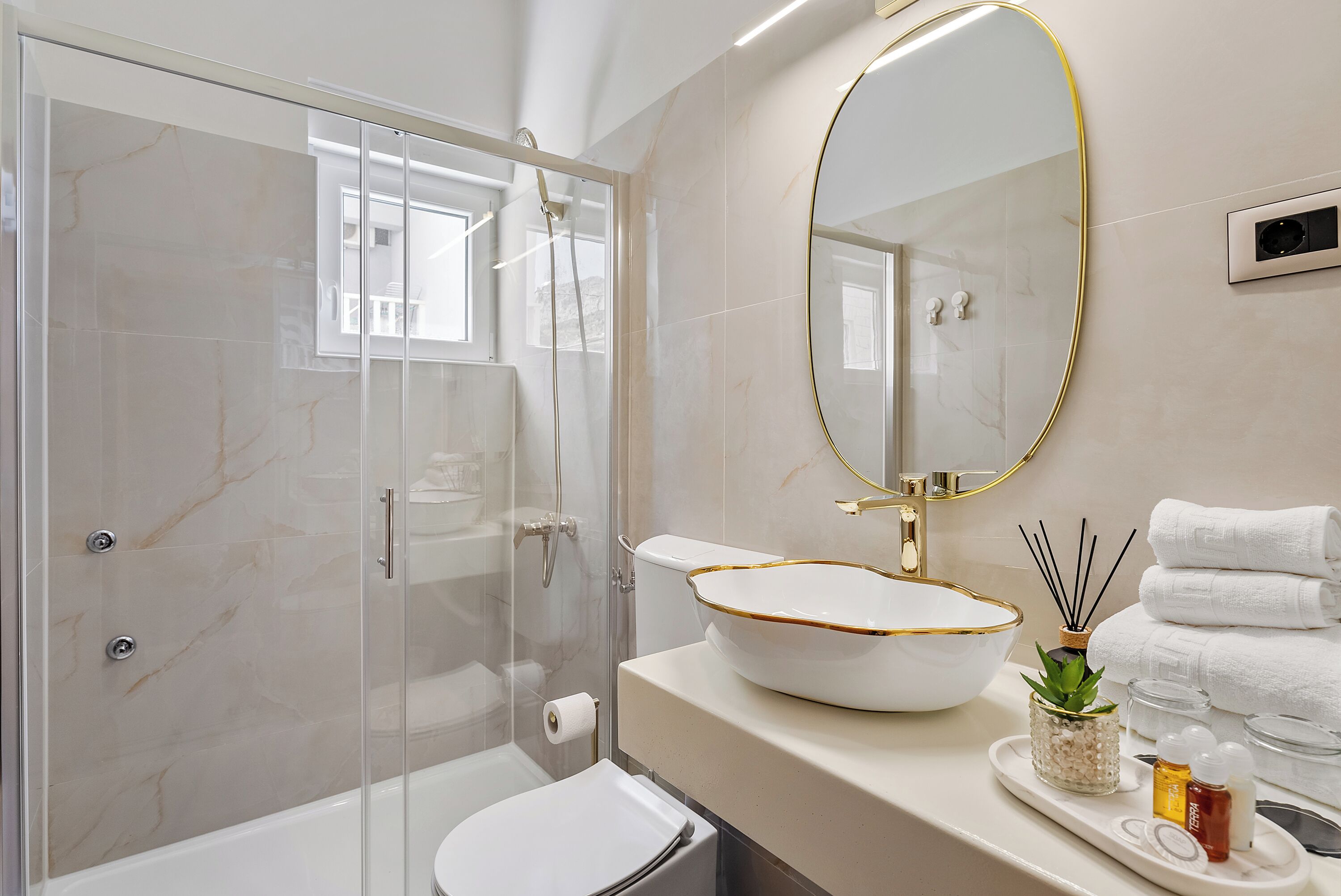 Een moderne badkamer met een douchecabine van glas, een wit wastafelmeubel met gouden rand en een grote spiegel.