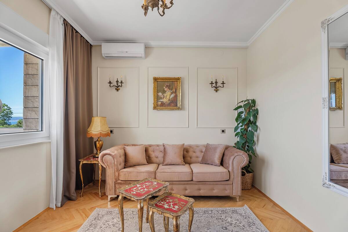 Una sala de estar con un sofá color crema, dos sillones a juego, una mesita con una lámpara, una planta grande en maceta y un espejo.