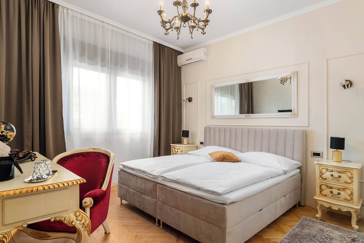 Habitación de hotel con cama doble, escritorio con silla, cómoda, espejo y candelabro.