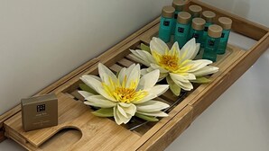 Un plateau en bois contenant un savon et deux fleurs artificielles, accompagné de six flacons de couleur turquoise avec des bouchons marron.