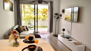 Un salon moderne comprenant un coin repas, un canapé, un téléviseur et un balcon agrémenté de plantes.