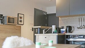 Una cocina moderna con microondas, cafetera y hervidor en la encimera. Hay un armario de madera y un lavabo con grifo.