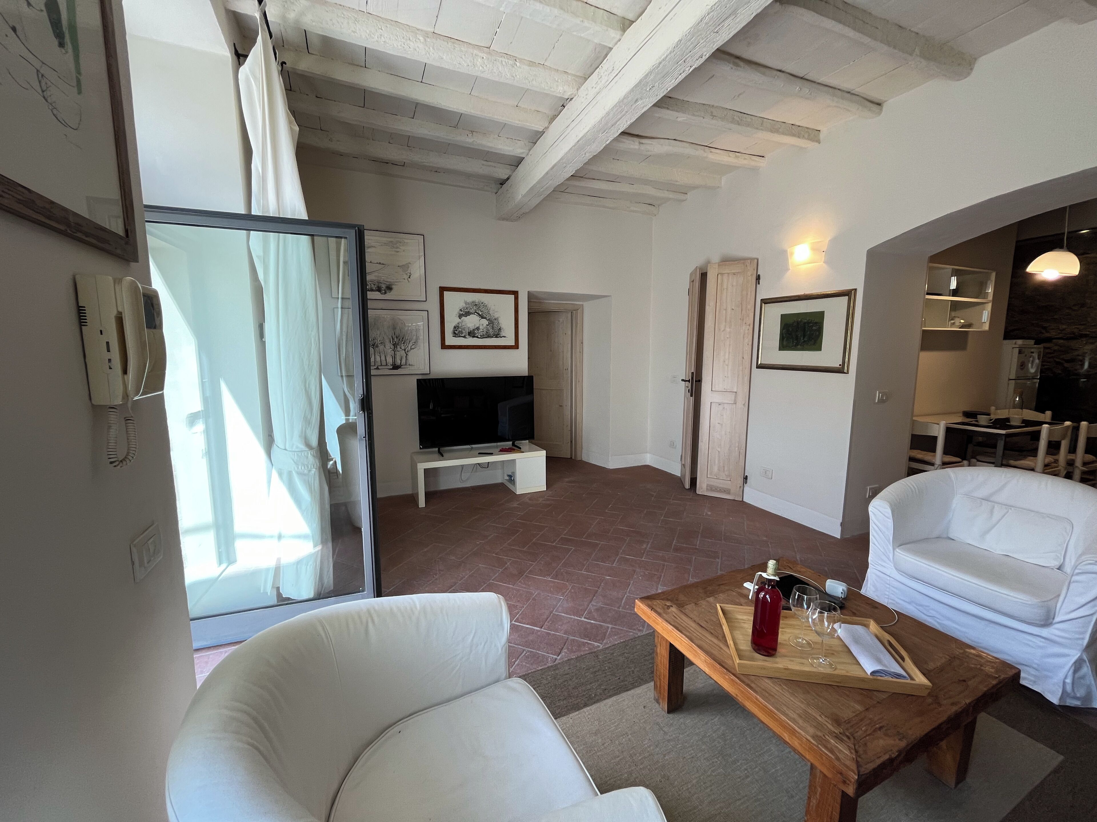 A living room with a TV, white sofas, a wooden coffee table, and a dining area with chairs.