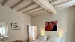 A bedroom with a large bed, a wooden door, a small table with a towel and a book, and a painting on the wall. - Your Terrace in Fiesole (Fiesole)
