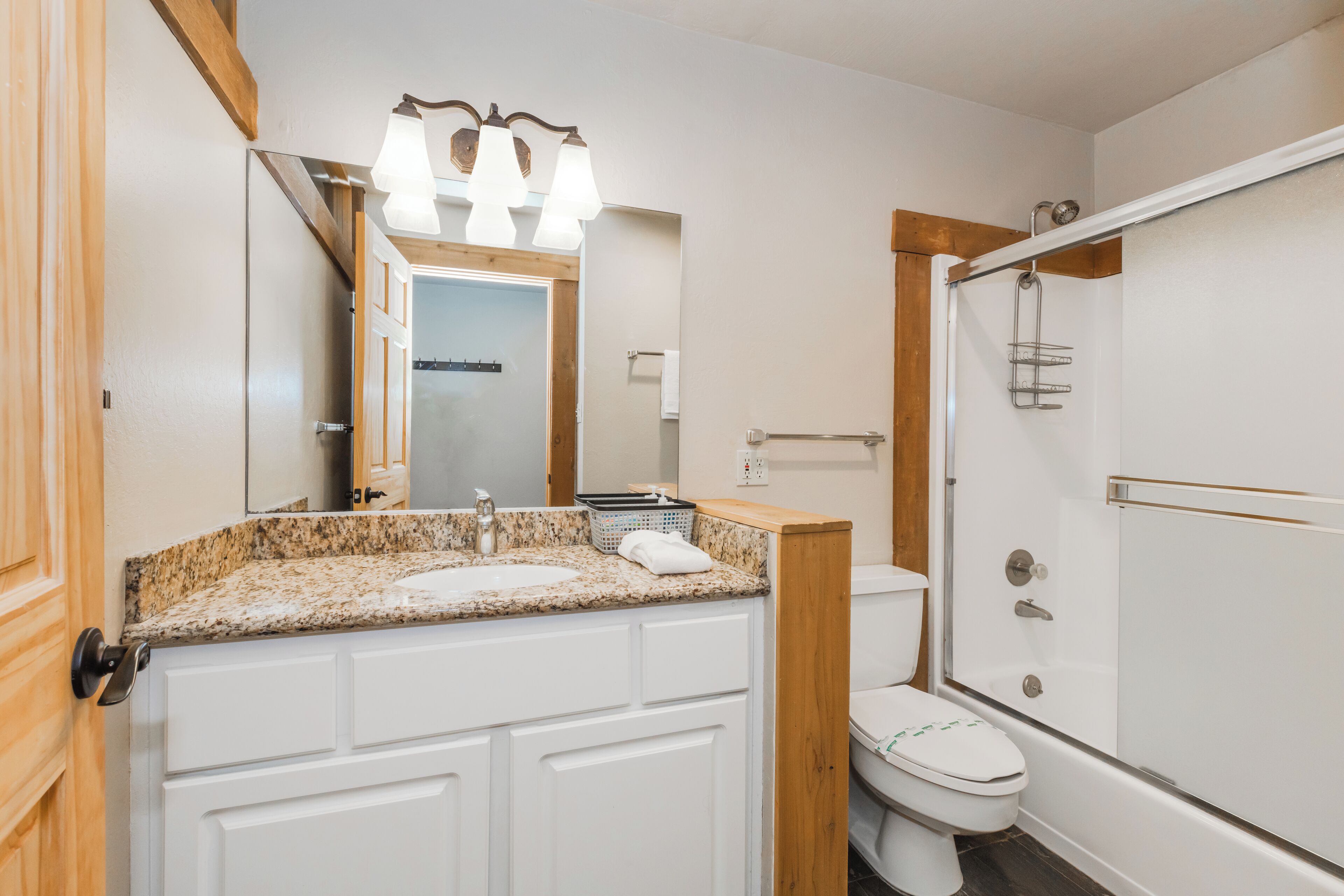 Une salle de bain avec un lavabo sur un plan de travail en granit, des toilettes blanches, une douche à parois de verre et un meuble-lavabo en bois.