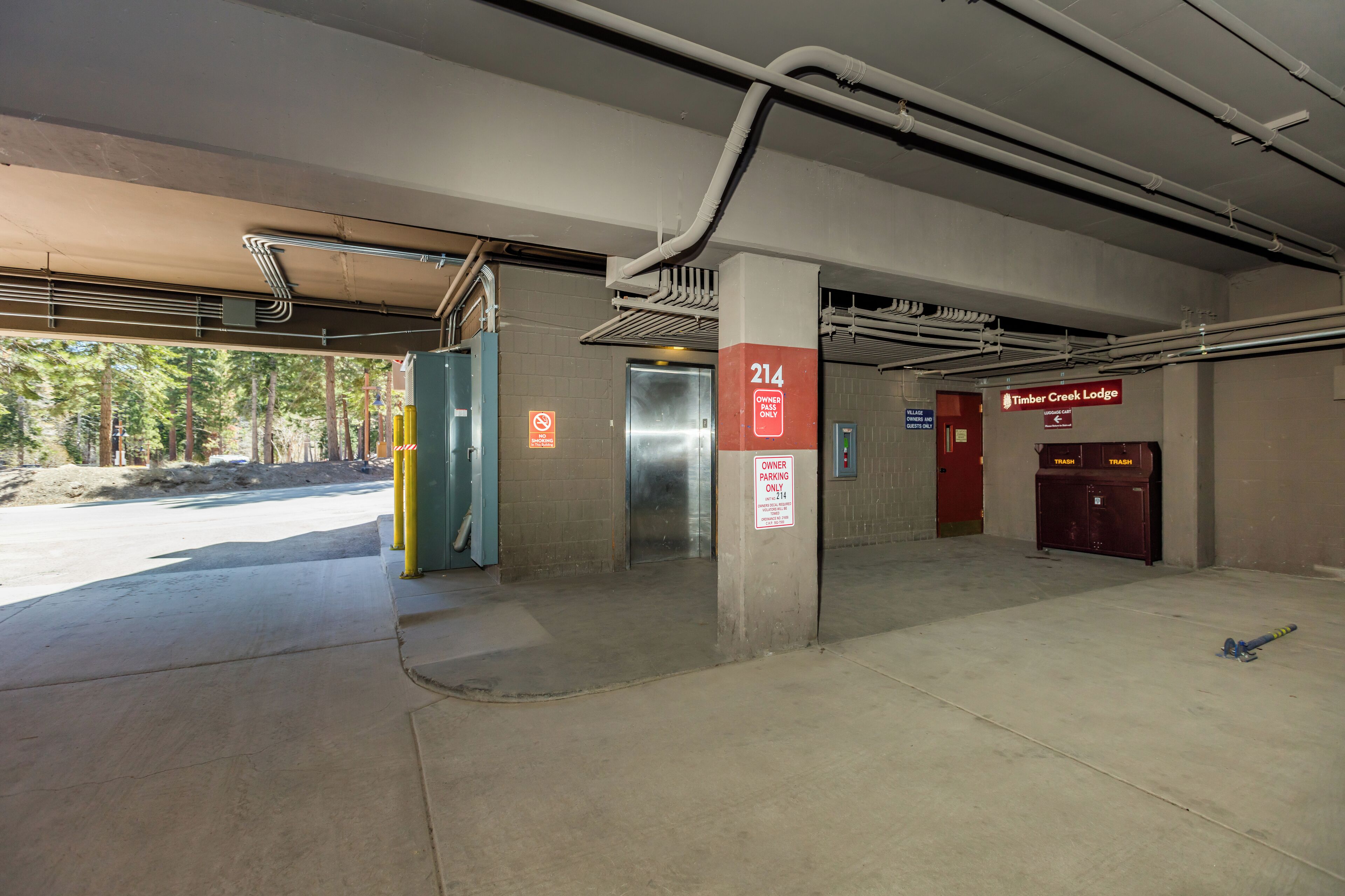 An underground parking area with a '214' elevator, a 'Timber Creek Lodge' sign, and a 'No Parking' sign.