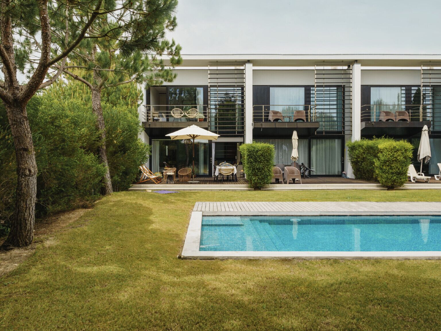 A modern two-story house with a swimming pool, outdoor seating, and a well-maintained lawn.