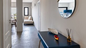 Un couloir avec un grand miroir rond, une petite table ornée d’objets décoratifs, un canapé et une vue sur un balcon.