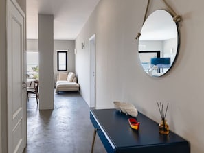 A hallway with a round mirror, a small table with decorative items, a sofa, and a view of a balcony.