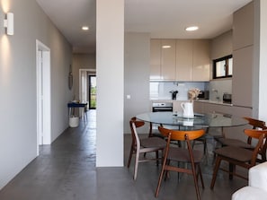 A modern kitchen with a glass dining table and wooden chairs, a white door, and a view into a dining area.