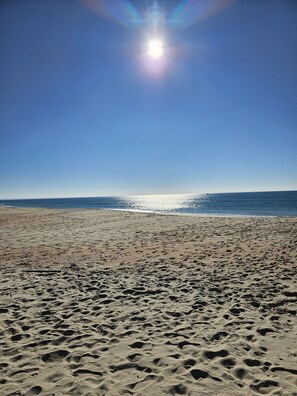 A beach with footprints, a clear sky, and the sun shining.