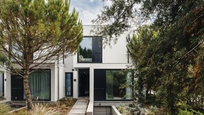 A modern two-story house with large glass windows, a concrete pathway, and surrounding greenery.