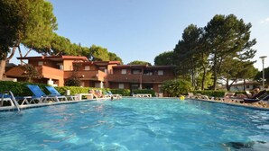 A swimming pool with lounge chairs and a building with multiple balconies in the background. - Family escape in Bibione (Bibione)
