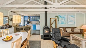 A spacious living area with a fireplace, a dining table with chairs, a sofa, and a kitchen in the background. - Awesome home in Rødby with sauna (Rødby)