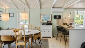 A dining area with a round table and chairs, a white cabinet with drawers, and a kitchen area with a counter and chairs. - Awesome home in Rødby with sauna (Rødby)