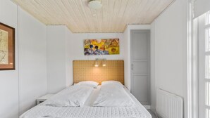 A bedroom with a wooden headboard, a bed with white bedding, a framed map on the wall, and a colorful abstract painting above the bed. - Awesome home in Rødby with sauna (Rødby)
