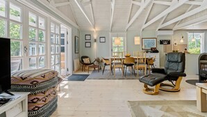 A spacious living room with a high ceiling, large windows, a dining area, and a seating area with a black leather chair. - Awesome home in Rødby with sauna (Rødby)