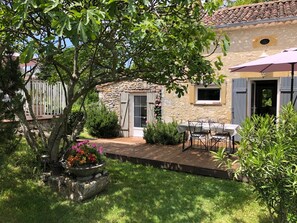 A stone house with a patio, a table and chairs, and a small garden area. - Hameau de 3 Maisons Individuelles en Pierre Avec Piscine à Débordement (Lolme)
