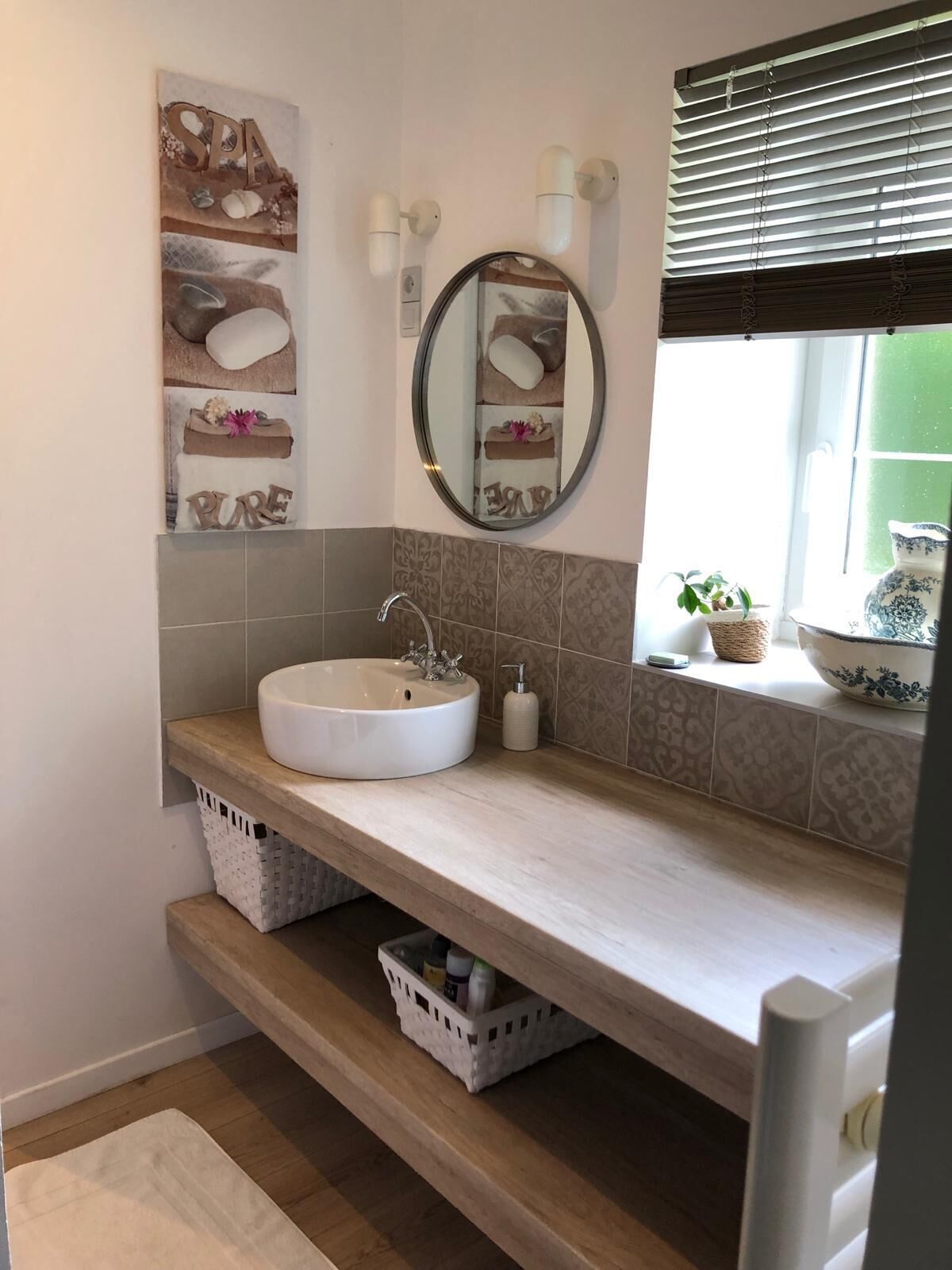 A bathroom with a round sink, a mirror, and a window with blinds.