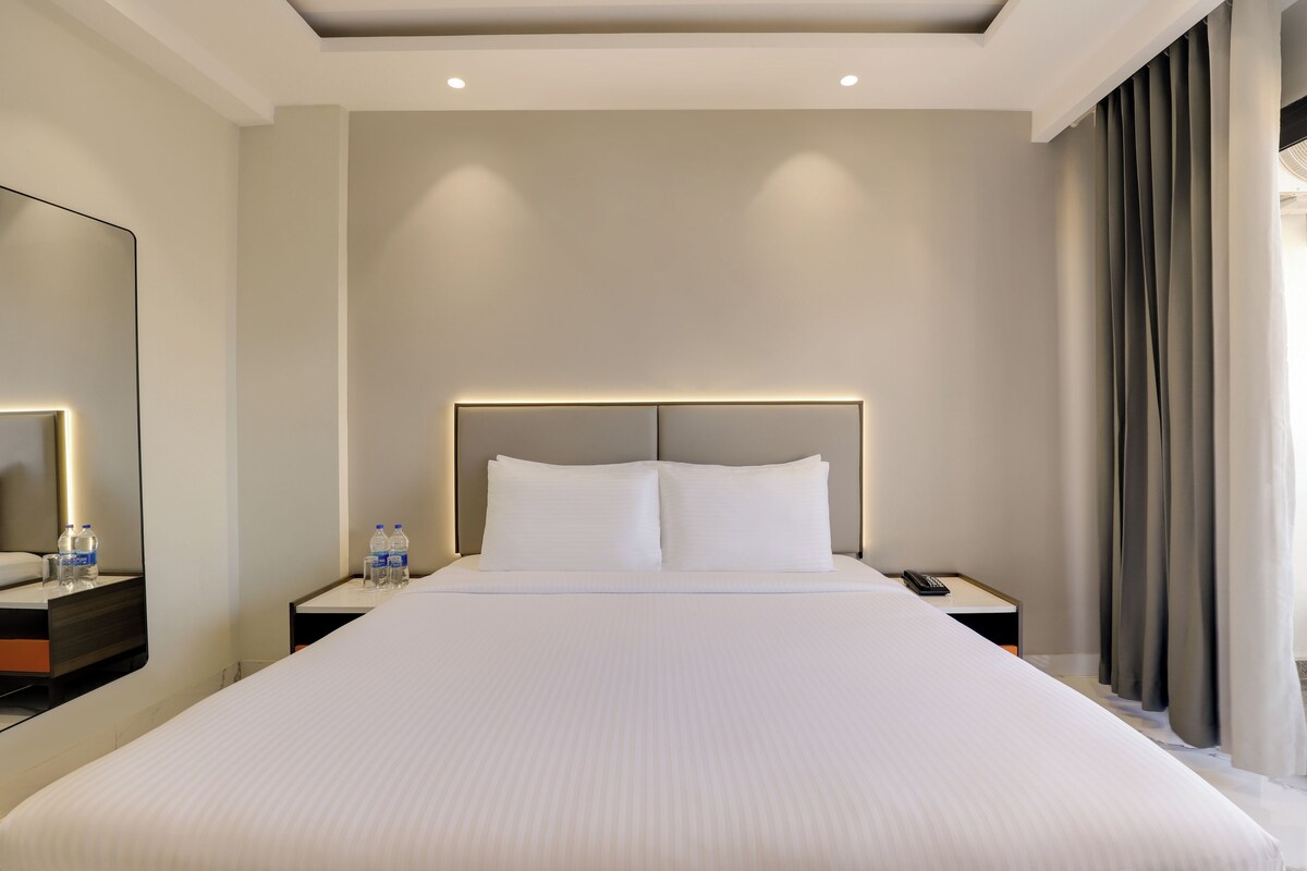 Een groot bed met hoofdbord, twee nachtkastjes, een spiegel en een bijzettafeltje met een telefoon en waterflessen.