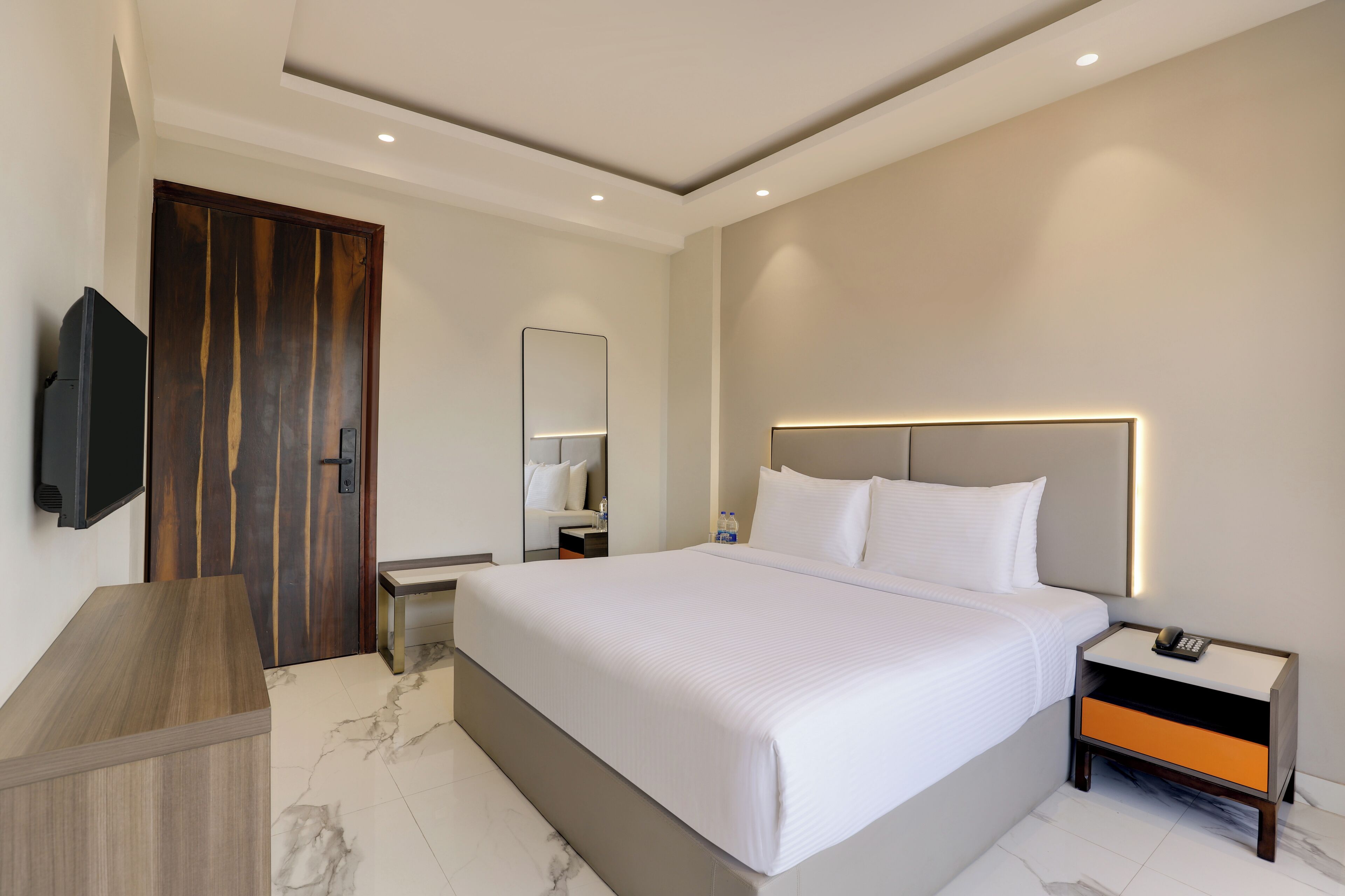 Una habitación de hotel moderna con una cama grande, mesitas de noche, un televisor y una puerta de madera.