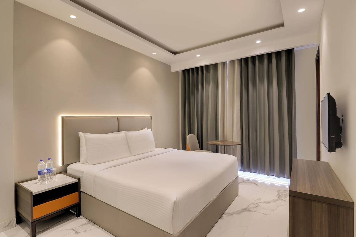 Une chambre d’hôtel moderne avec un grand lit, une table de chevet avec des bouteilles d’eau, une petite table et un téléviseur fixé au mur.