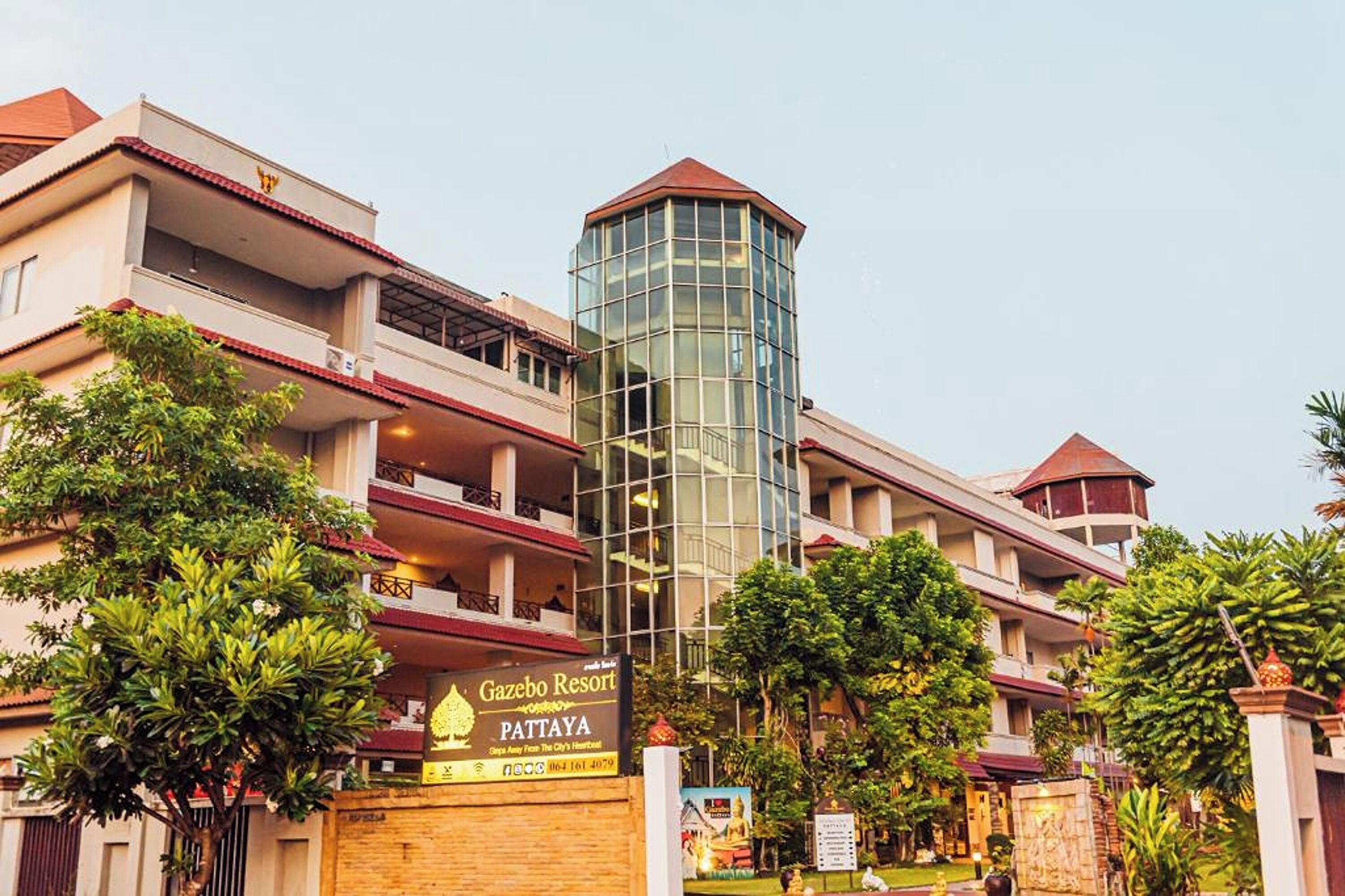 A multi-story hotel with a prominent glass tower, a sign for Gazebo Resort Pattaya, and lush greenery around the property.