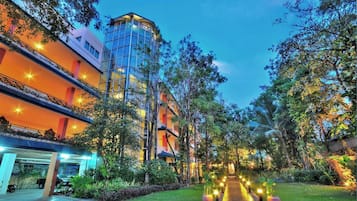A multi-story hotel with a glass facade, surrounded by lush greenery and illuminated pathways.
