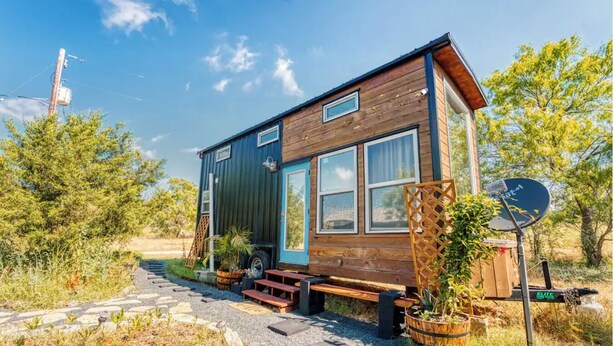 Une petite cabane en bois avec une véranda, une antenne parabolique et une échelle menant à une fenêtre.