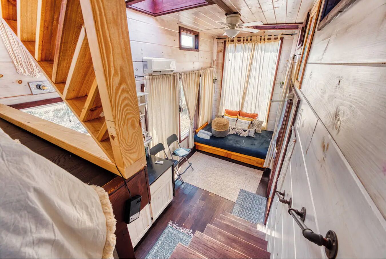 Ein gemütliches Blockhaus-Interieur mit einer Holztreppe, einer kleinen Sitzecke mit Kissen und einem Deckenventilator.
