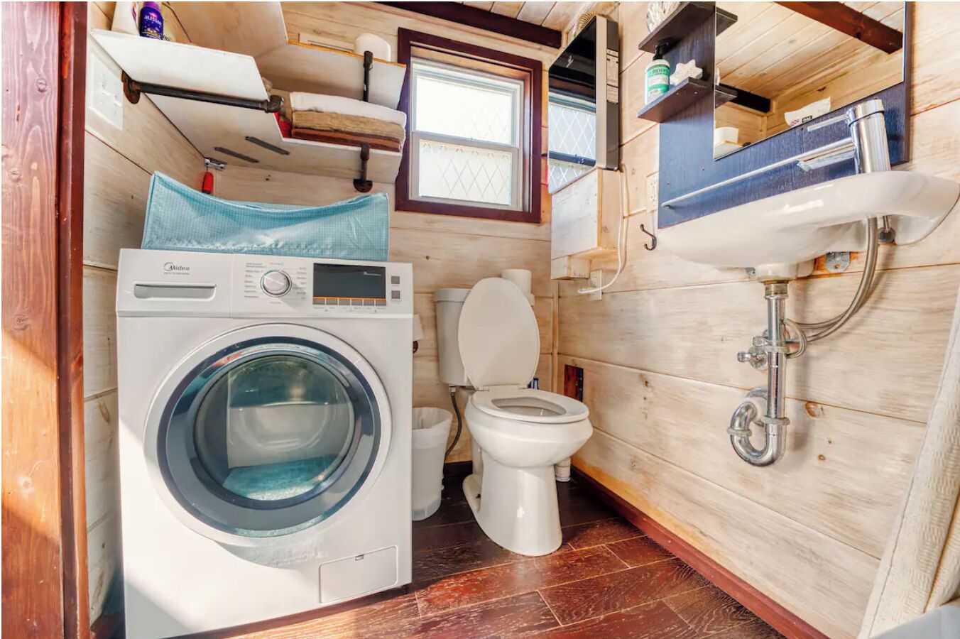 A compact, wooden interior with a washing machine, toilet, and a small window.
