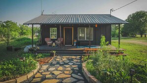 Une maison moderne dotée d’un porche abrité, de deux chaises, d’une table et d’un chemin de jardin menant à l’entrée.